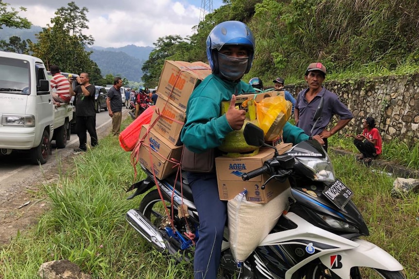 A man on a heavily laden motorcycle gives the thumbs up