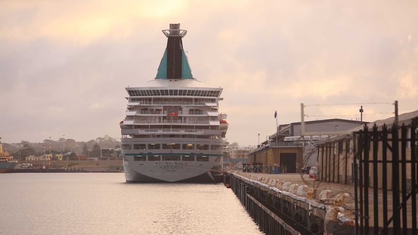 The cruise ship sits alongside the dock. It is early morning judging by the light.