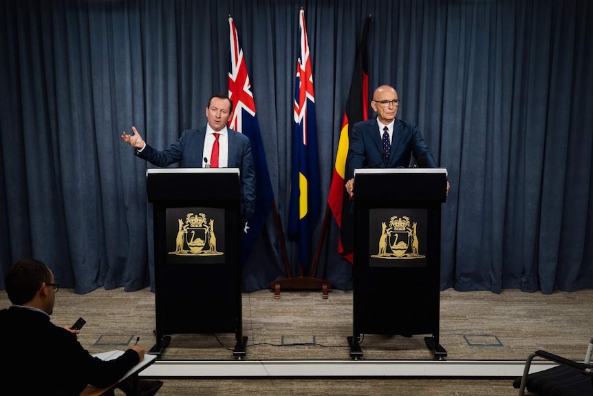 Mark McGowan and John Quigley standing side by side at podiums speaking to the media in front of flags.