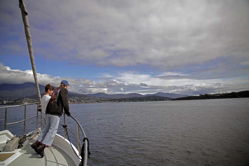 A wide shot of a boat on a river under cloudy skies showing a young woman and her younger brother looking over the side
