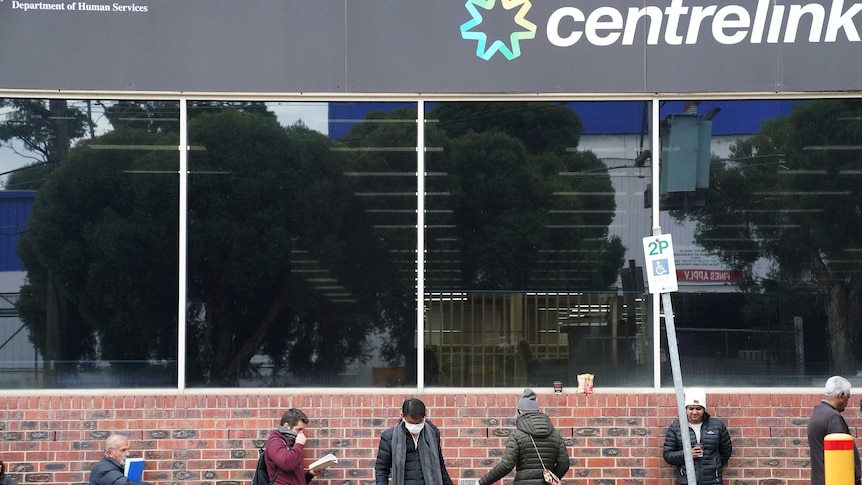 A line of people in front of a building with a sign that reads 'centrelink'.