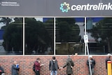 A line of people in front of a building with a sign that reads 'centrelink'.