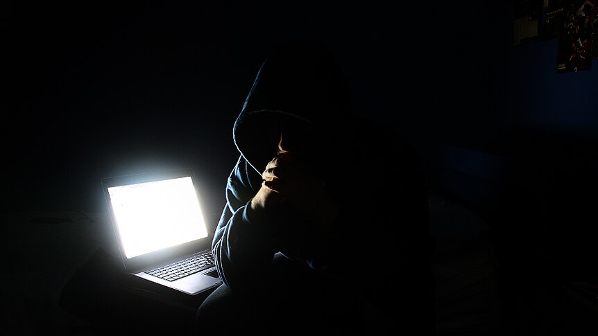 A man wearing a hood next to his laptop