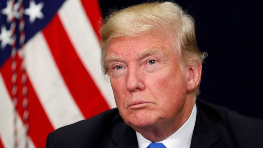 A close up of Trump in front of a flag