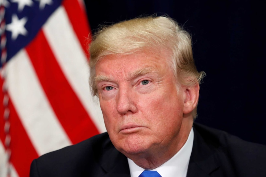 A close up of Trump in front of a flag