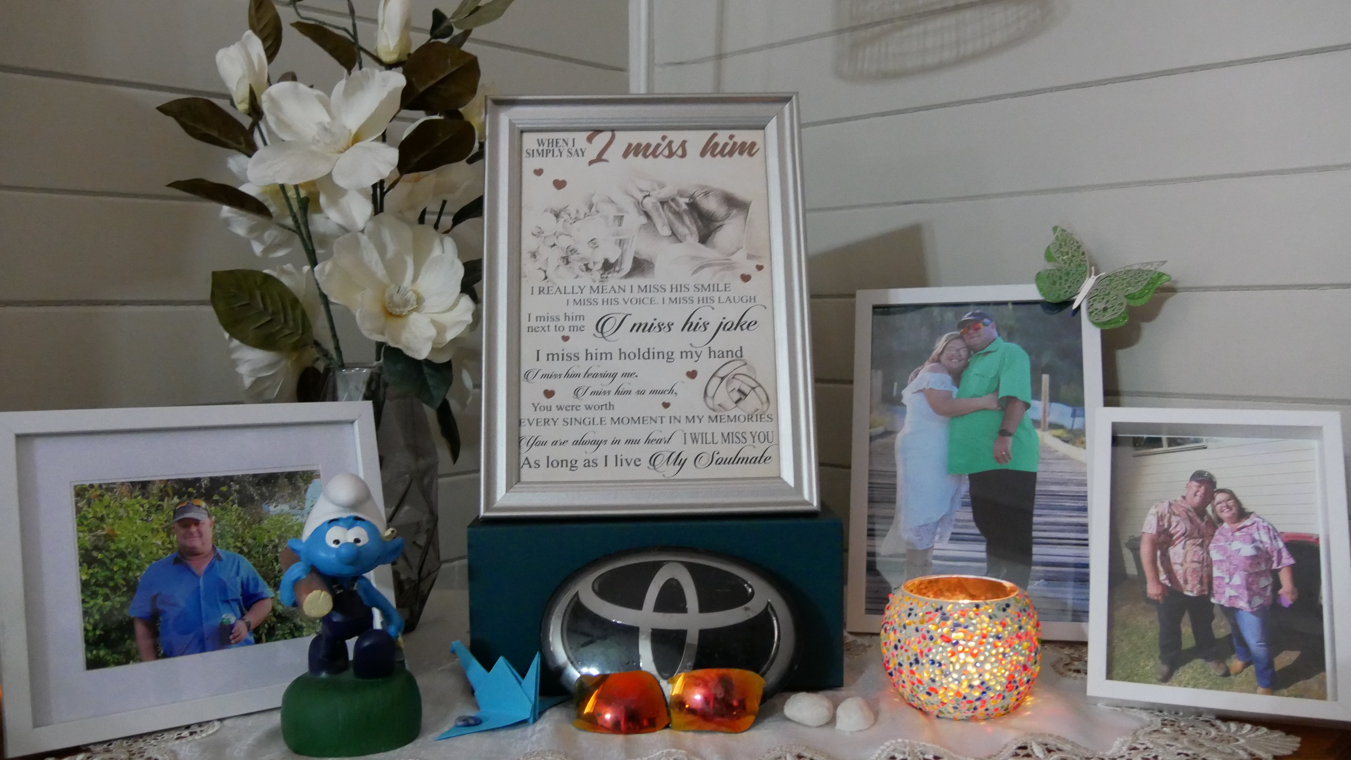 Um santuário contendo imagens de Troy Ernst, poemas, uma estátua de um Smurf e uma vela.