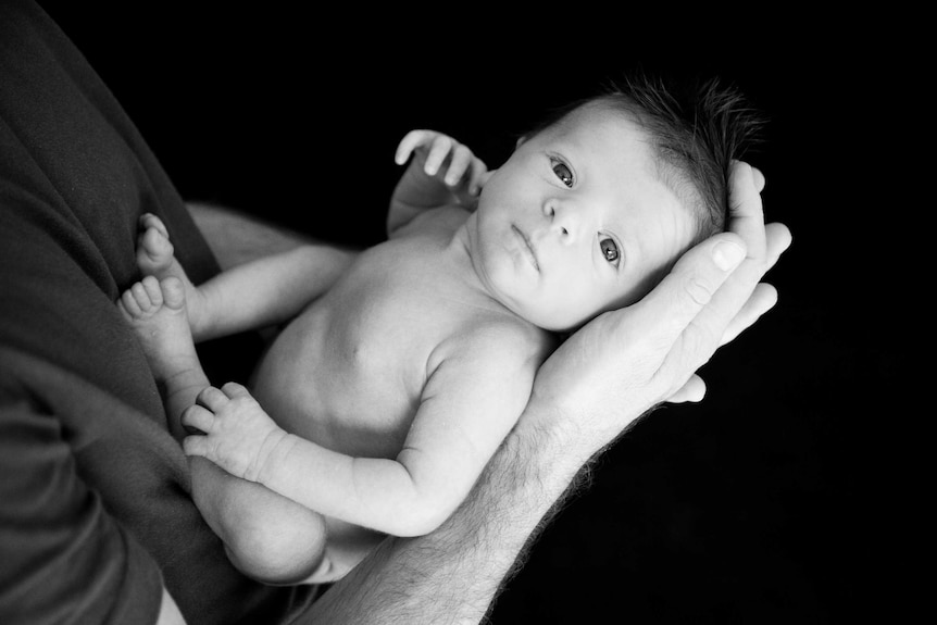Black and white portrait of a small baby boy nestled in his father's arms.