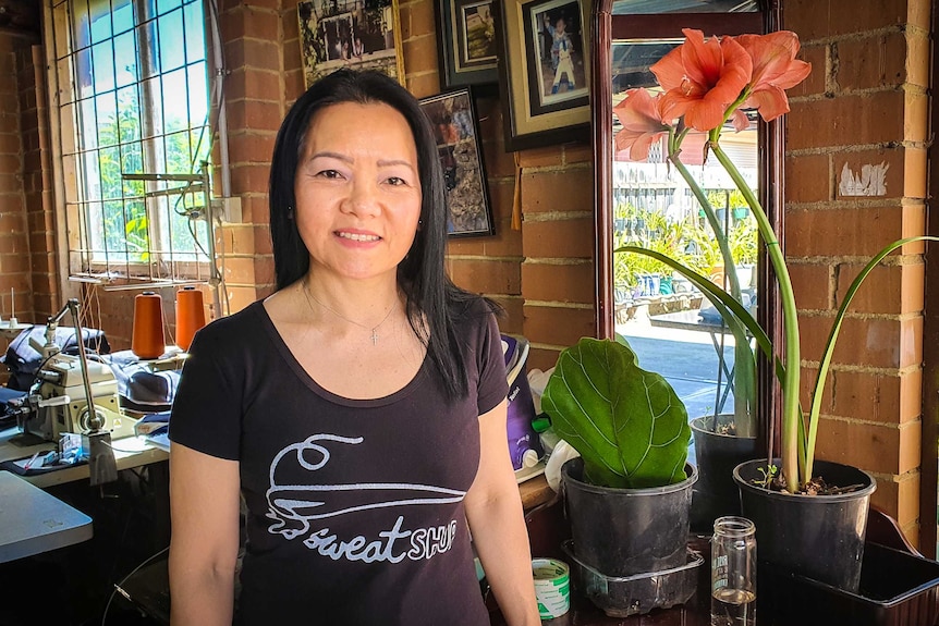 A woman standing in front of a wall with framed photos and plants