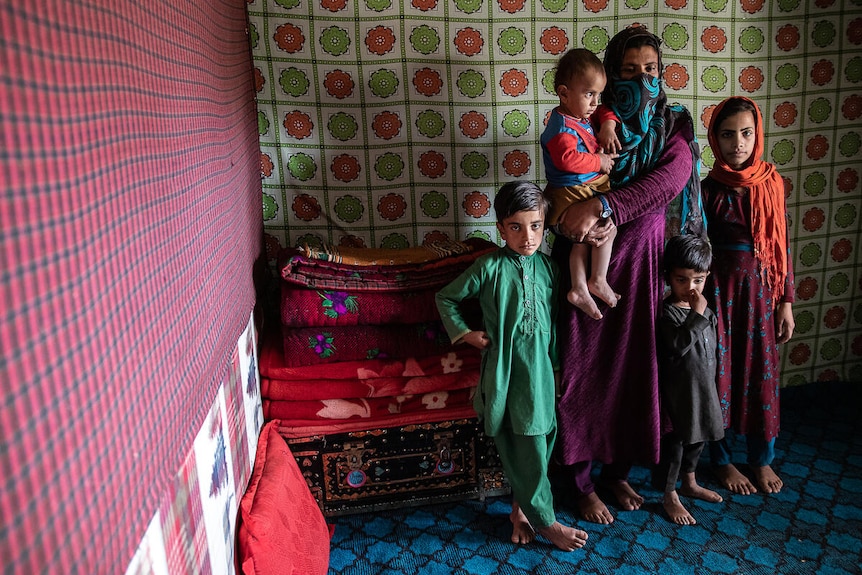 Children standing with their parent against a carpeted wall.