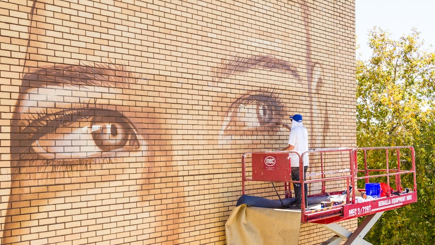 Street artist Rone paints a mural of a local woman in Benalla last year.