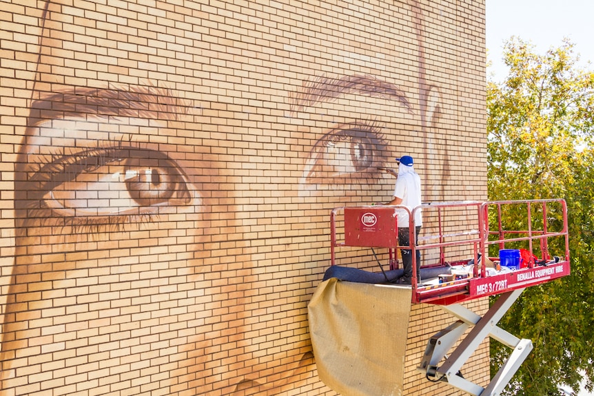 Street artist Rone paints a mural of a local woman in Benalla last year.