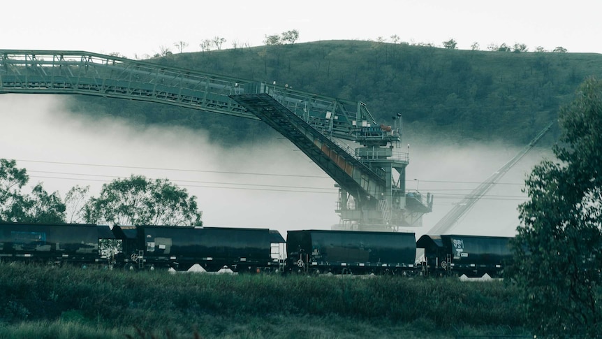 A line of coal train carriages in front of a coal washer machine which is partially covered in fog.