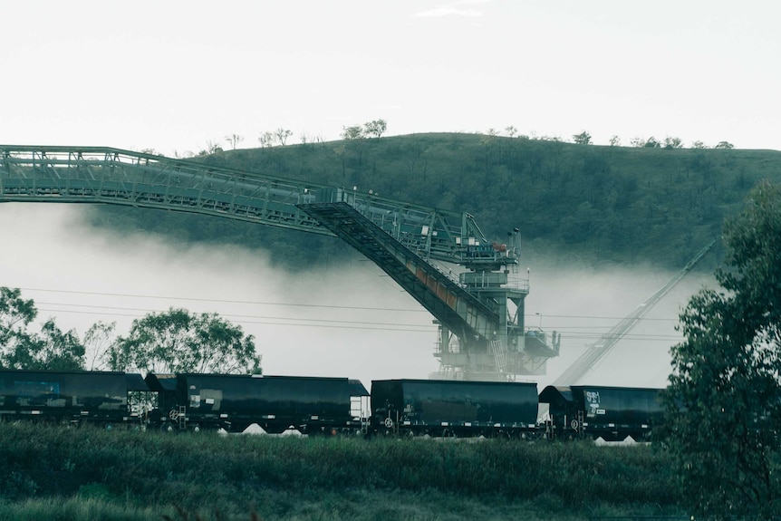 A line of coal train carriages in front of a coal washer machine which is partially covered in fog.