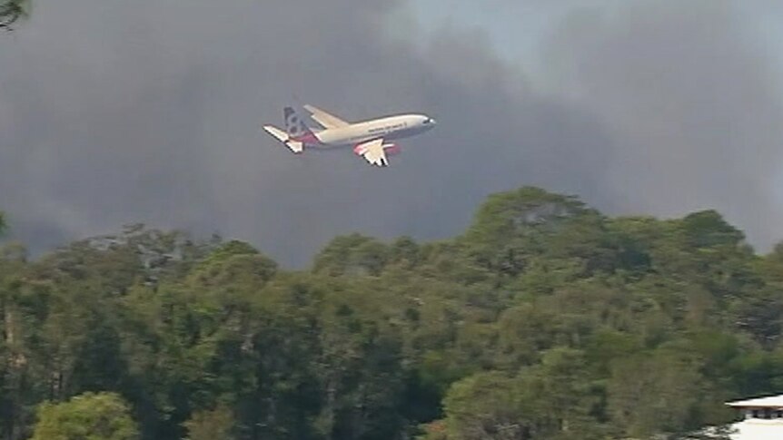 A 737 flying at low altitude over tree tops through bushfire smoke