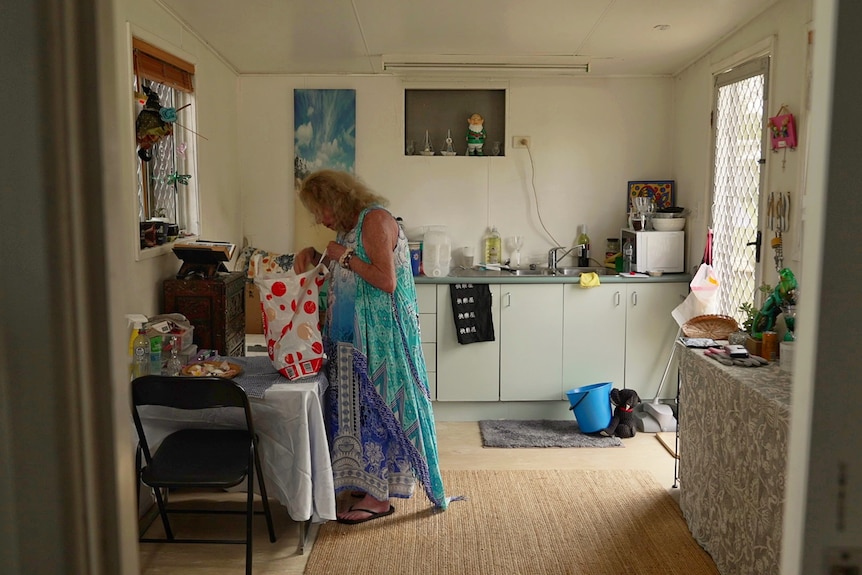A woman looks inside a plastic shopping bag in a small kitchen area.