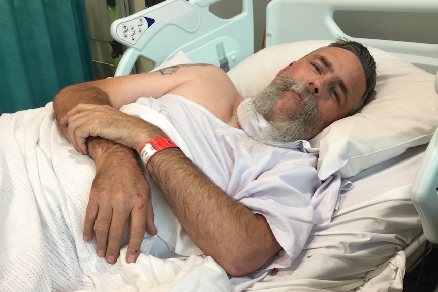Man laying in a hospital bed holding his arm.