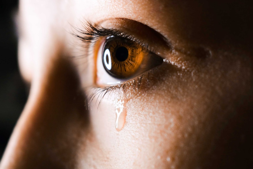 A close up of a woman's eye with a tear running down her cheek.