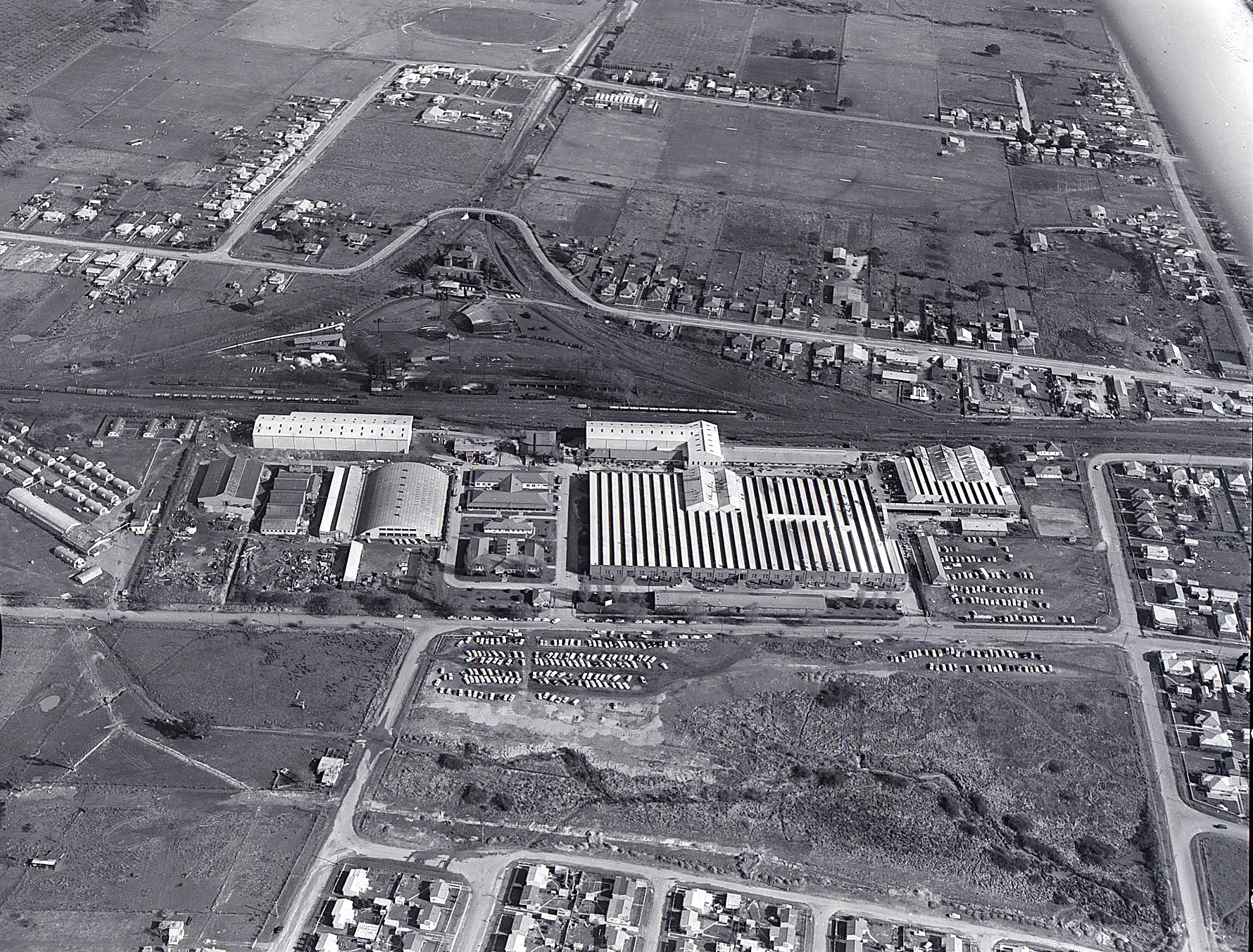 A black and white aerial shot of a factory surrounded by roads, houses and vacant land