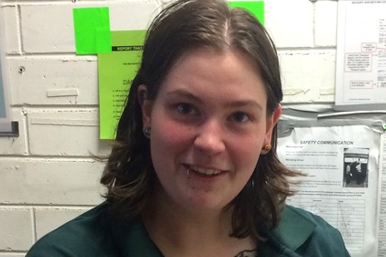 A headshot of Jemma Lilley in front of a white brick wall, wearing a green shirt.