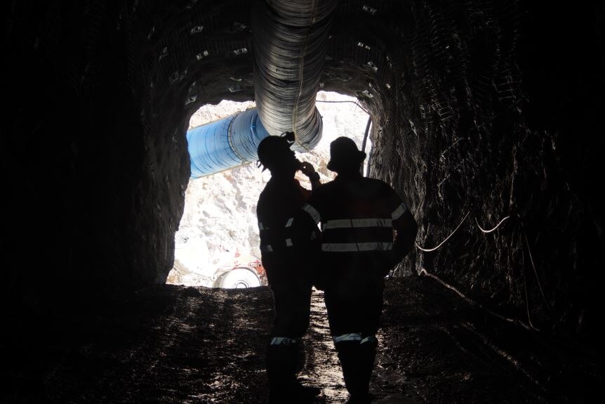Two men silhouetted standing at the entrance to an underground mine.