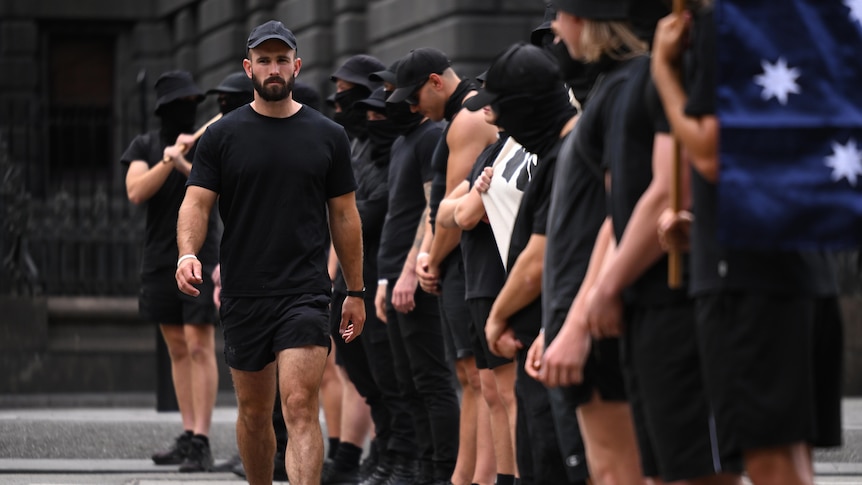 A man wearing all black walks along a line of other men, also wearing black.
