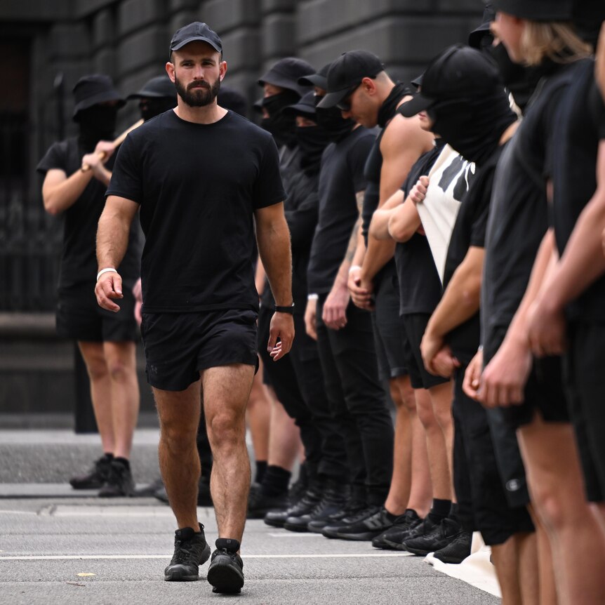 A man wearing all black walks along a line of other men, also wearing black.