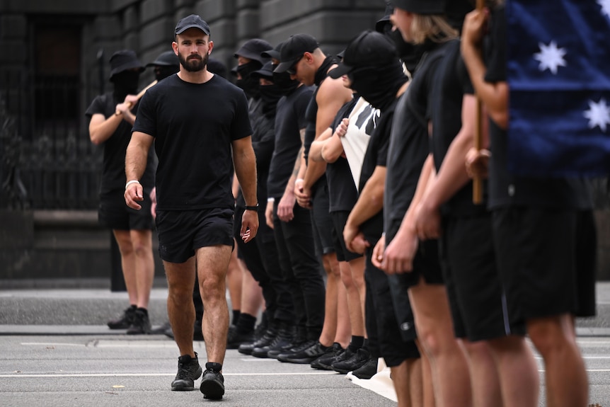 A man wearing all black walks along a line of other men, also wearing black.