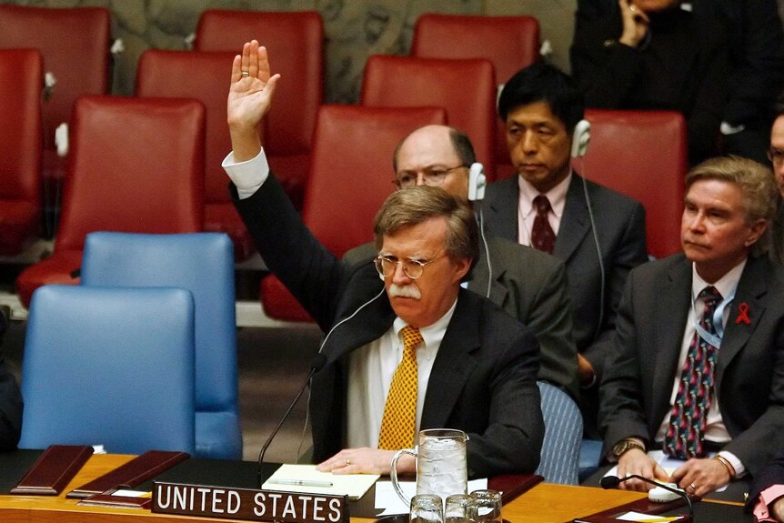 An image from 2006 of John Bolton sitting as his desk raising his hand to vote at the UN Headquarters