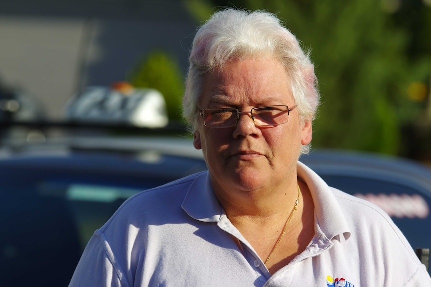 A tight head and shoulders shot of Deb Papamichael standing in front of her out-of-focus taxi.