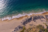 A drone shot with a birds eye view of blue waves crashing on Bunbury's Back Beach.
