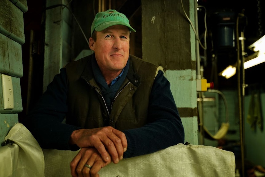 A man wearing a green cap, a vest and long-sleeved clothing smiles at the camera.