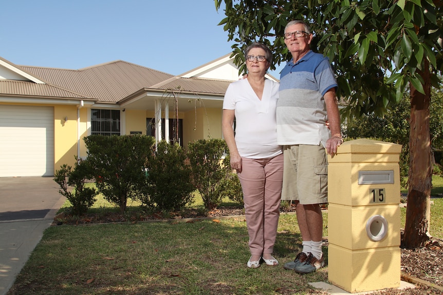 A middle-aged couple standing under a tree in front of a house.