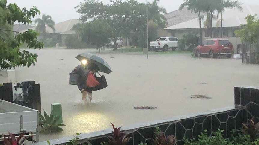 A person walking in pouring rain with umbrella in a flooded Townsville street.