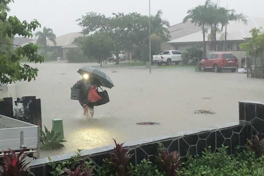 A person walking in pouring rain with umbrella in a flooded Townsville street.