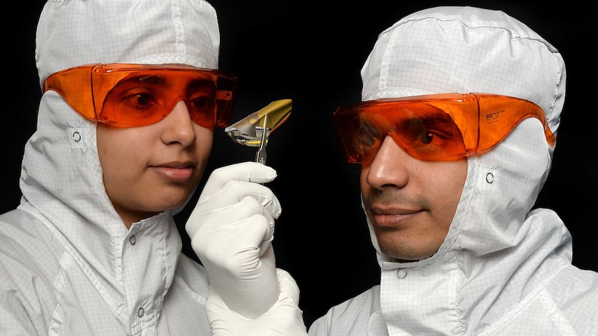 Professor Madhu Bhaskaran and Professor Sharath Sriram dressed in lab coats with orange safety goggles, looking at a metal