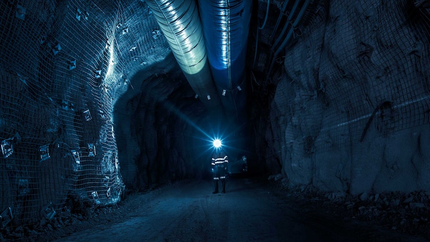 Gold mine worker standing underground in the dark illuminated by head lamp.