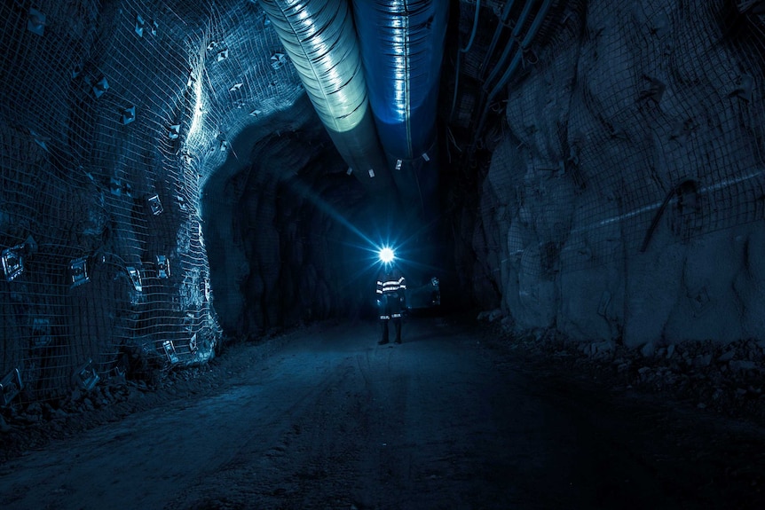 Gold mine worker standing underground in the dark illuminated by head lamp