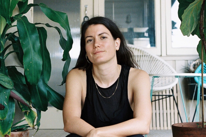 The artist Merinda Davies, a young woman in black with a gold necklace sitting on the steps of an old Qlder house