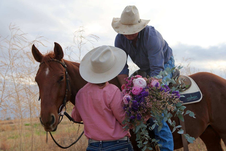 Belinda Murphy being given a large bunch of pink and purple flowers from her husband who's on a horse.