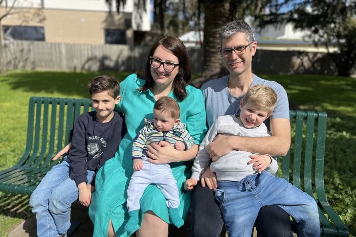 Pam pictured with her three kids and husband sitting on a park bench.
