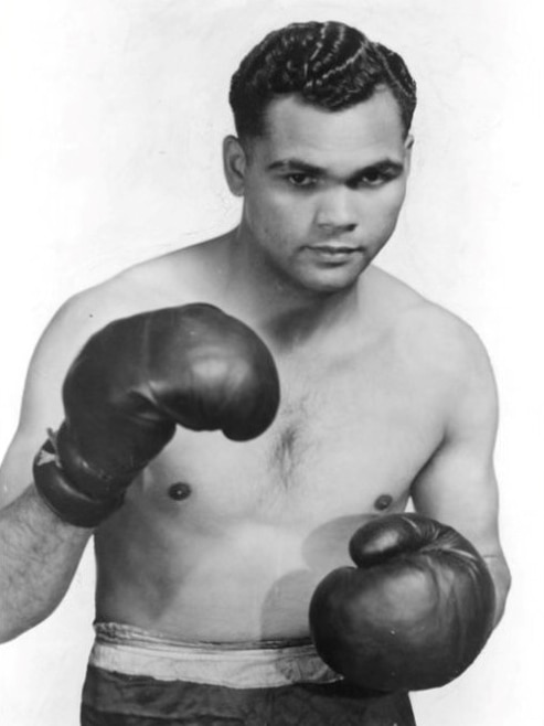 A black and white image of a young boxer, in boxing shorts and gloves.