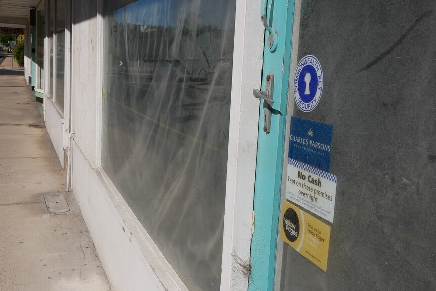 The dusty door of a shop front, with dusty covered-up windows stretching down the street.