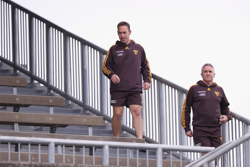 Two men in brown clothes walking down a grandstand.