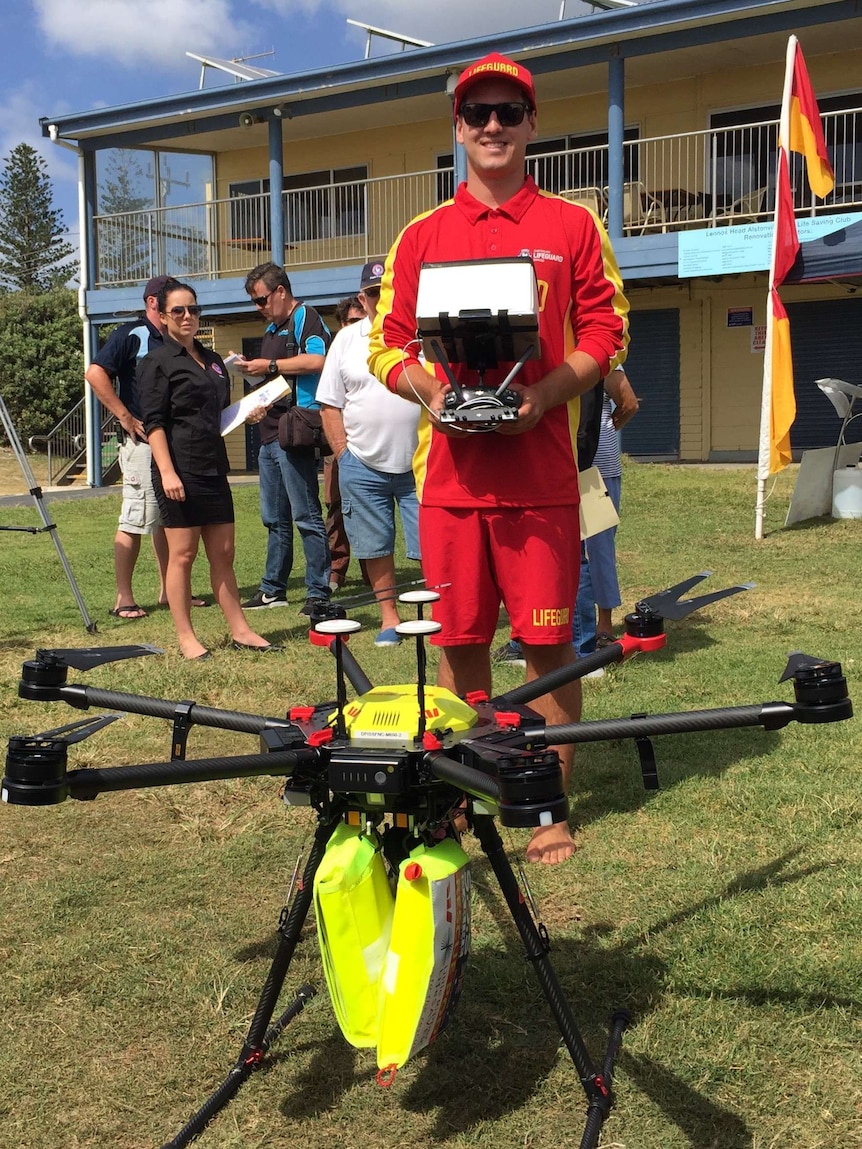 A surf lifesaver holding the control box and standing behind a drone.