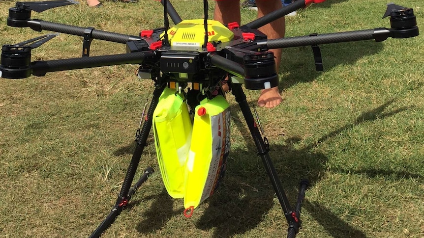 A surf lifesaver holding the control box and standing behind a drone.