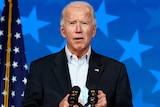 Joe Biden speaking at a lectern with a microphone infront of him and an american flag behind