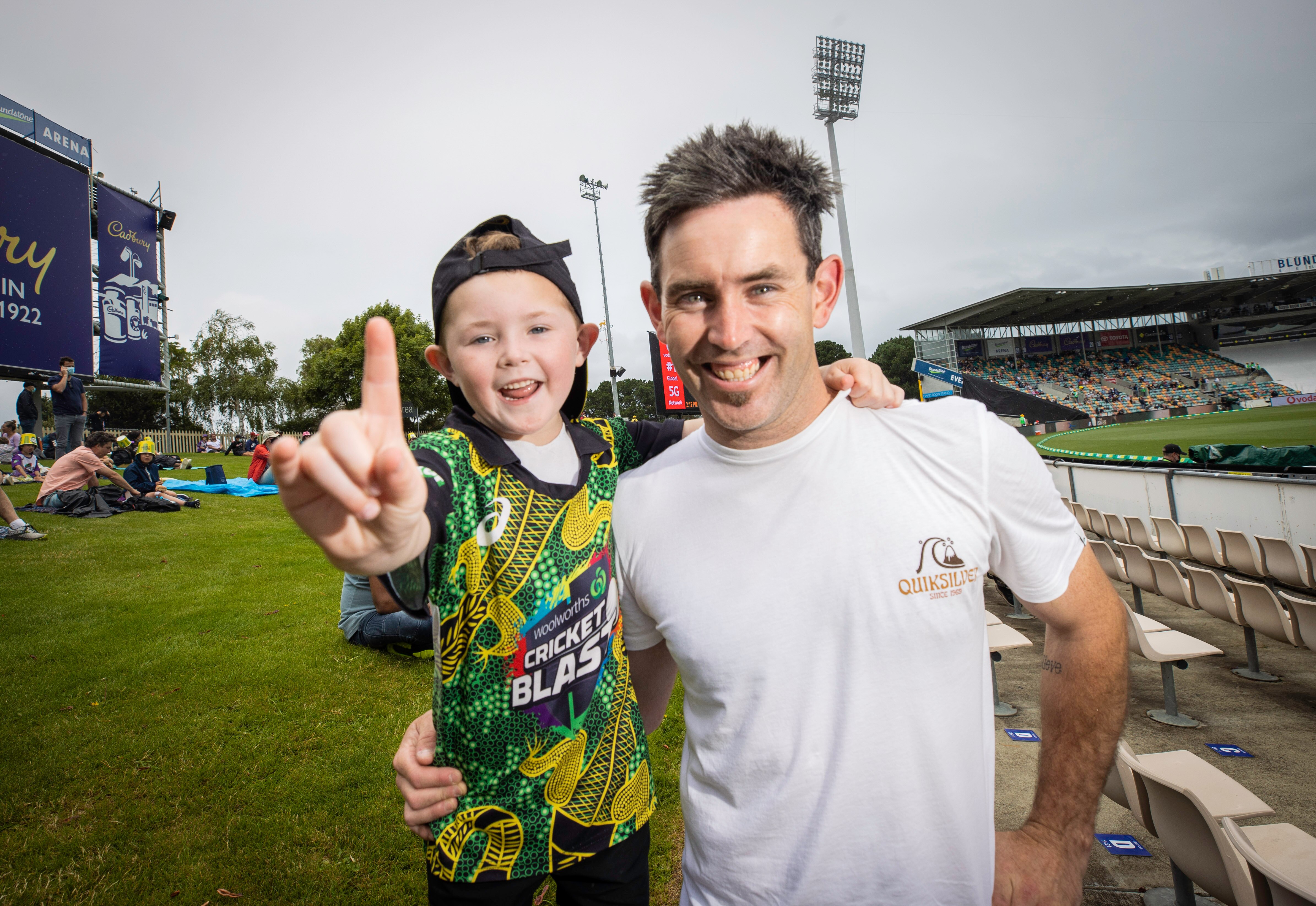 A young boy wearing a cap backwards smiles with his father at a cricket oval.