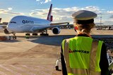 A pilot in a cap and high-vis vest looks from a platform at a Qantas A380 at an airport in the sunrise.