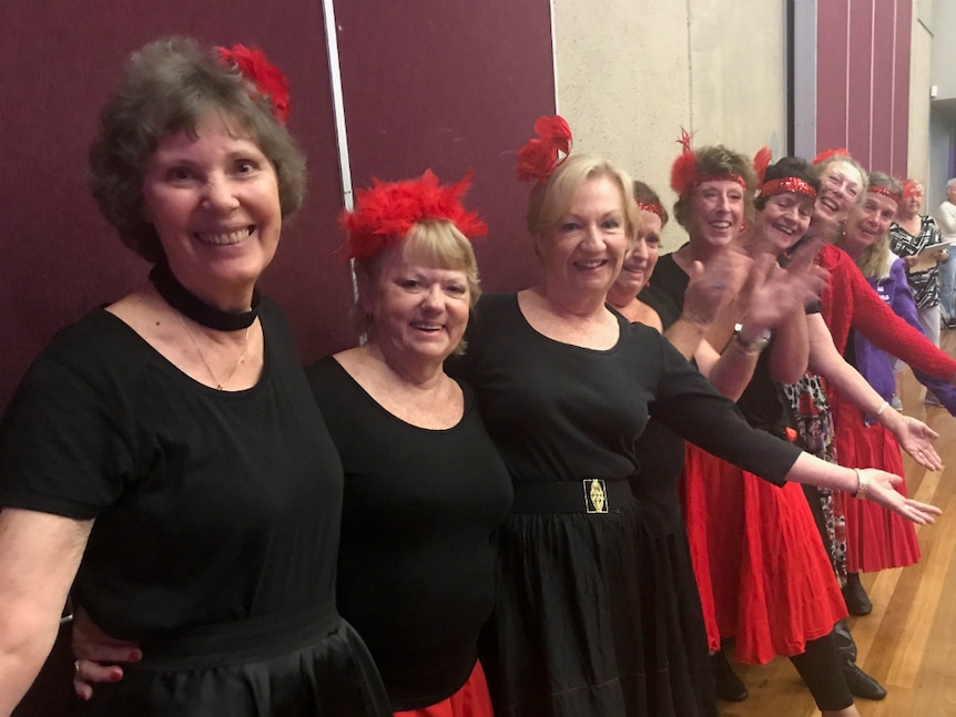 A line of older women, dressed up in basic costumes smiling and looking at the camera.