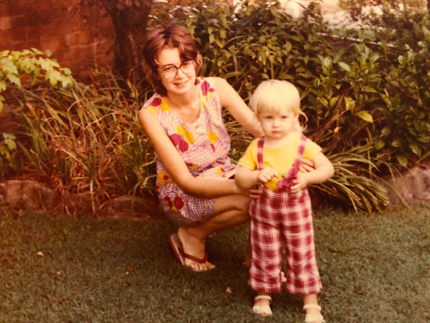 A woman smiles with a child in a garden